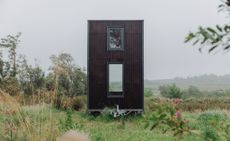 An upright metal container turned into a mobile home with two windows