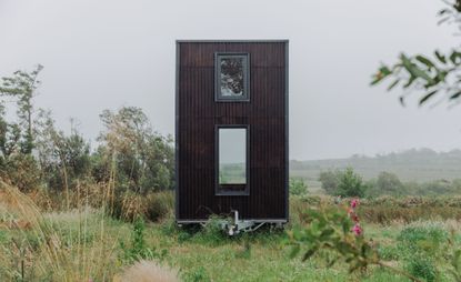 An upright metal container turned into a mobile home with two windows