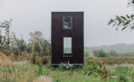 An upright metal container turned into a mobile home with two windows