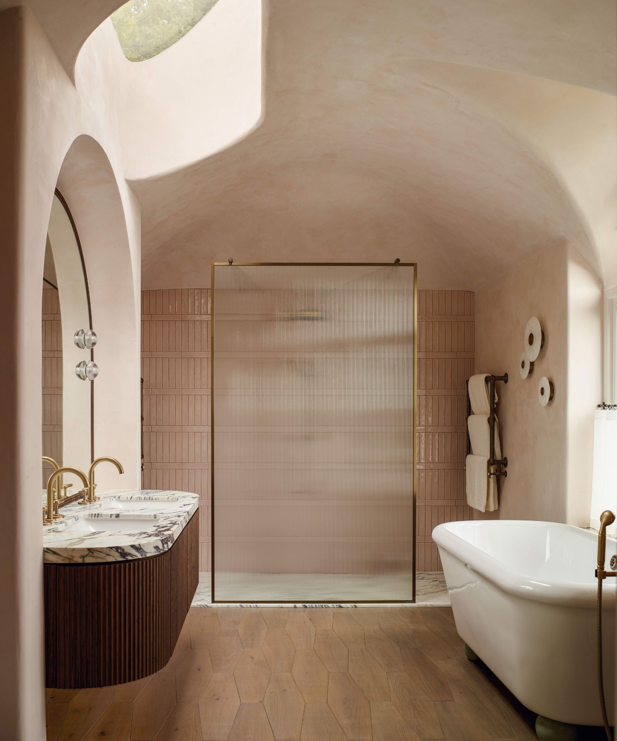 a curved pink plastered main bathroom with a sky light, reeded shower screen, curved bathtub and floating vanity