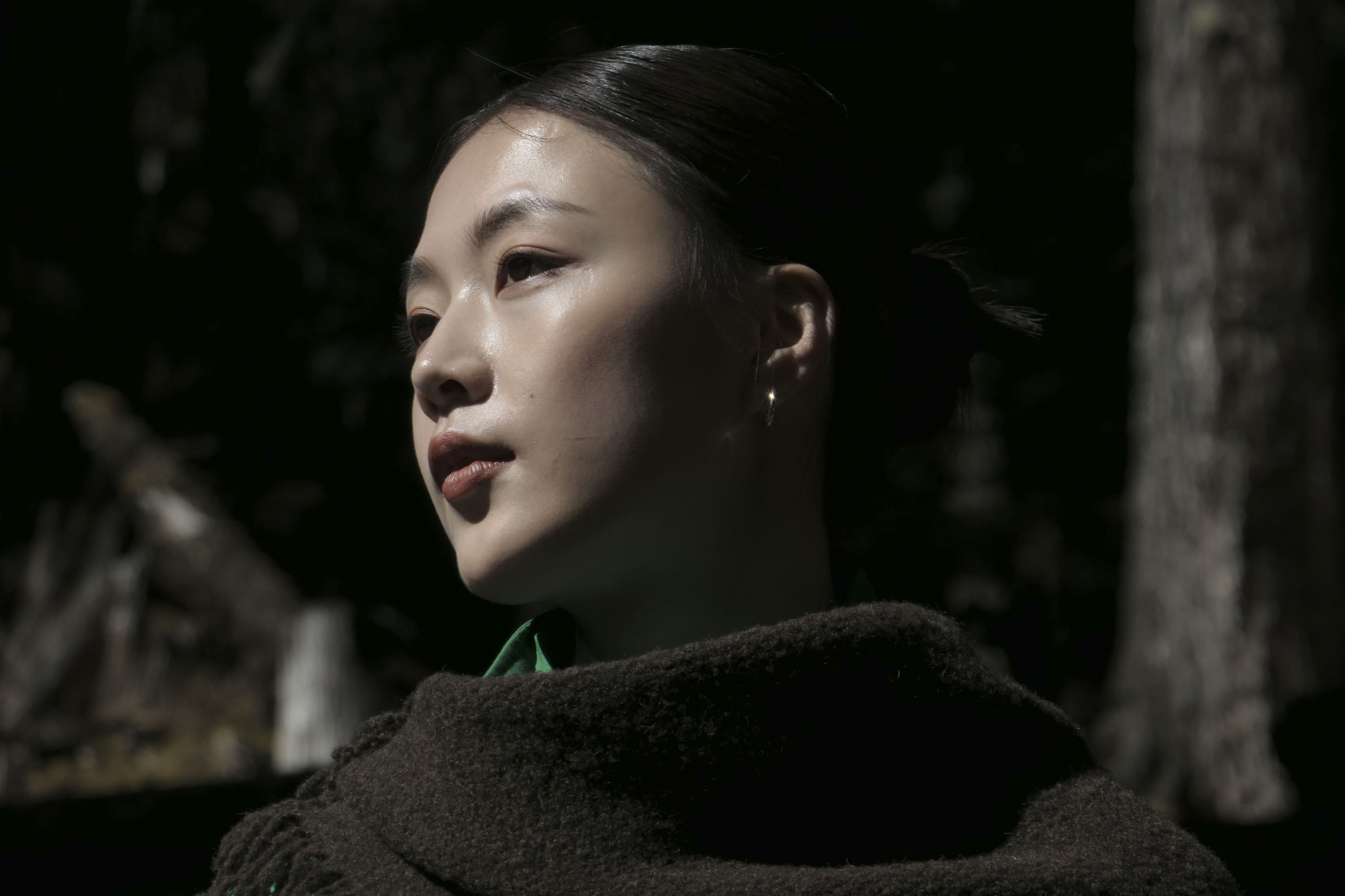 Portrait of a woman in a shawl and green jacket in a woodland, there's direct sunlight on her