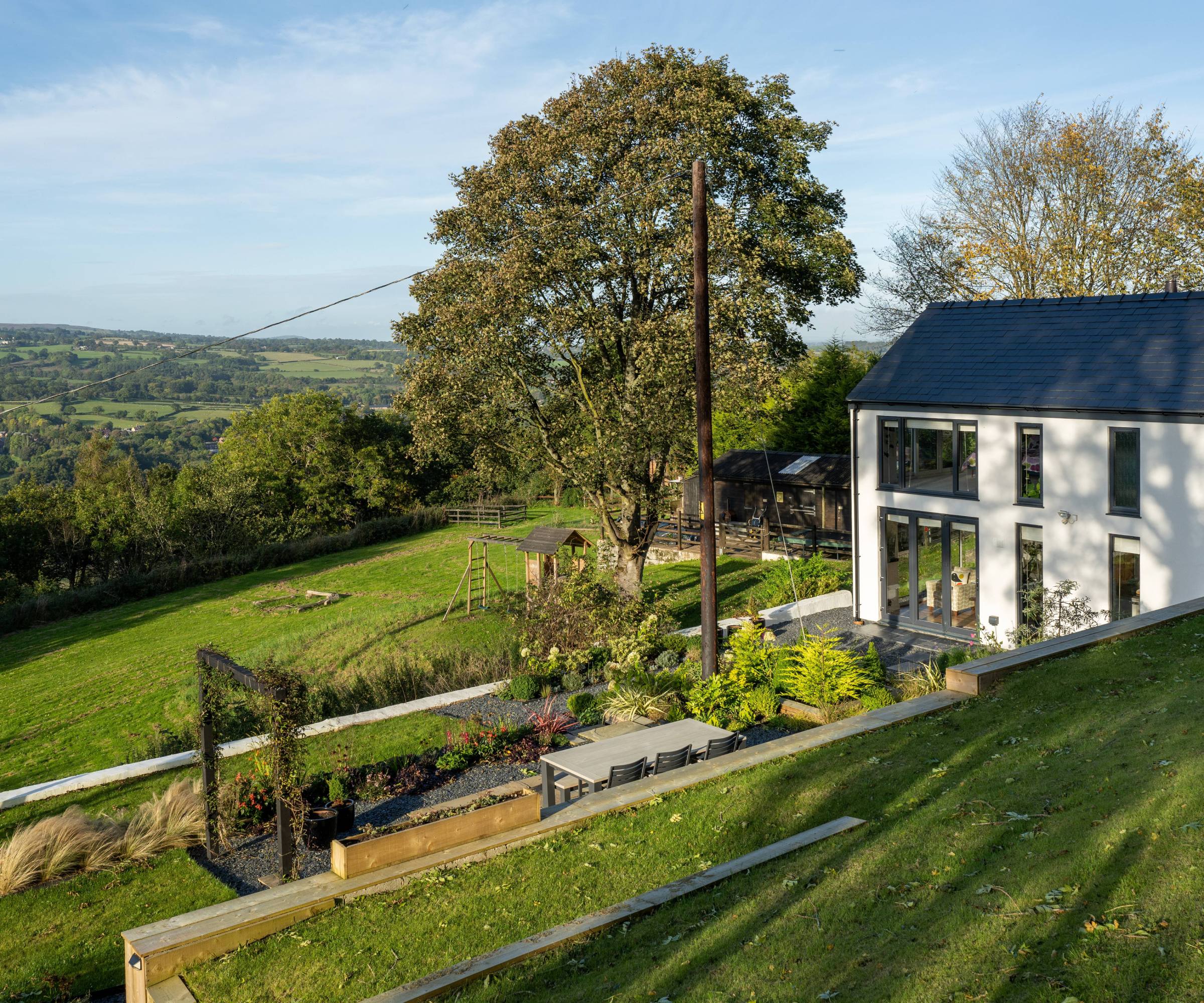 White stone cottage in Welsh countryside with modern extension featuring landscaping and scenic valley views