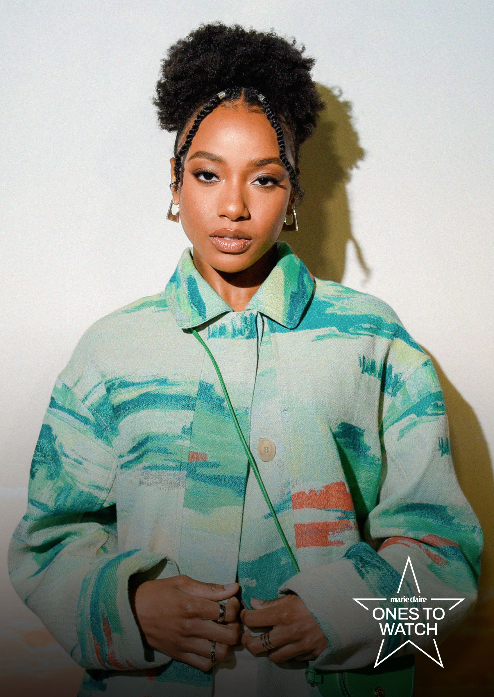 actress and theater producer alyah chanelle scott poses against a white backdrop wearing a printed green coat