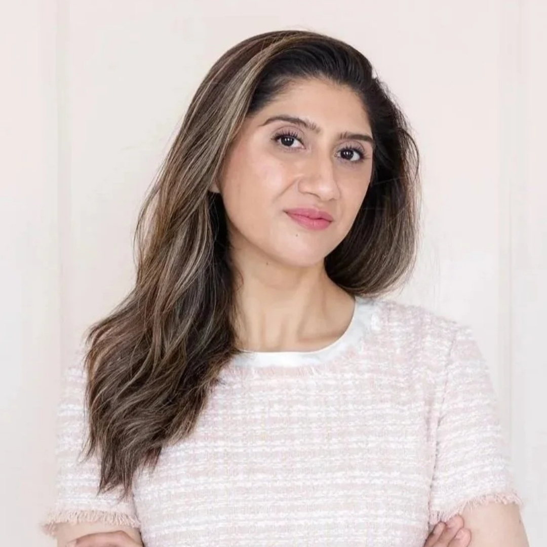 Image of Dr Sidra Khan smiling with long wavy brunette hair and wearing a pink check dress
