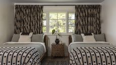 A bedroom with two twin beds, a patterned throw on the beds, and retro patterned curtains in the window