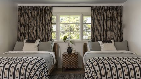 A bedroom with two twin beds, a patterned throw on the beds, and retro patterned curtains in the window