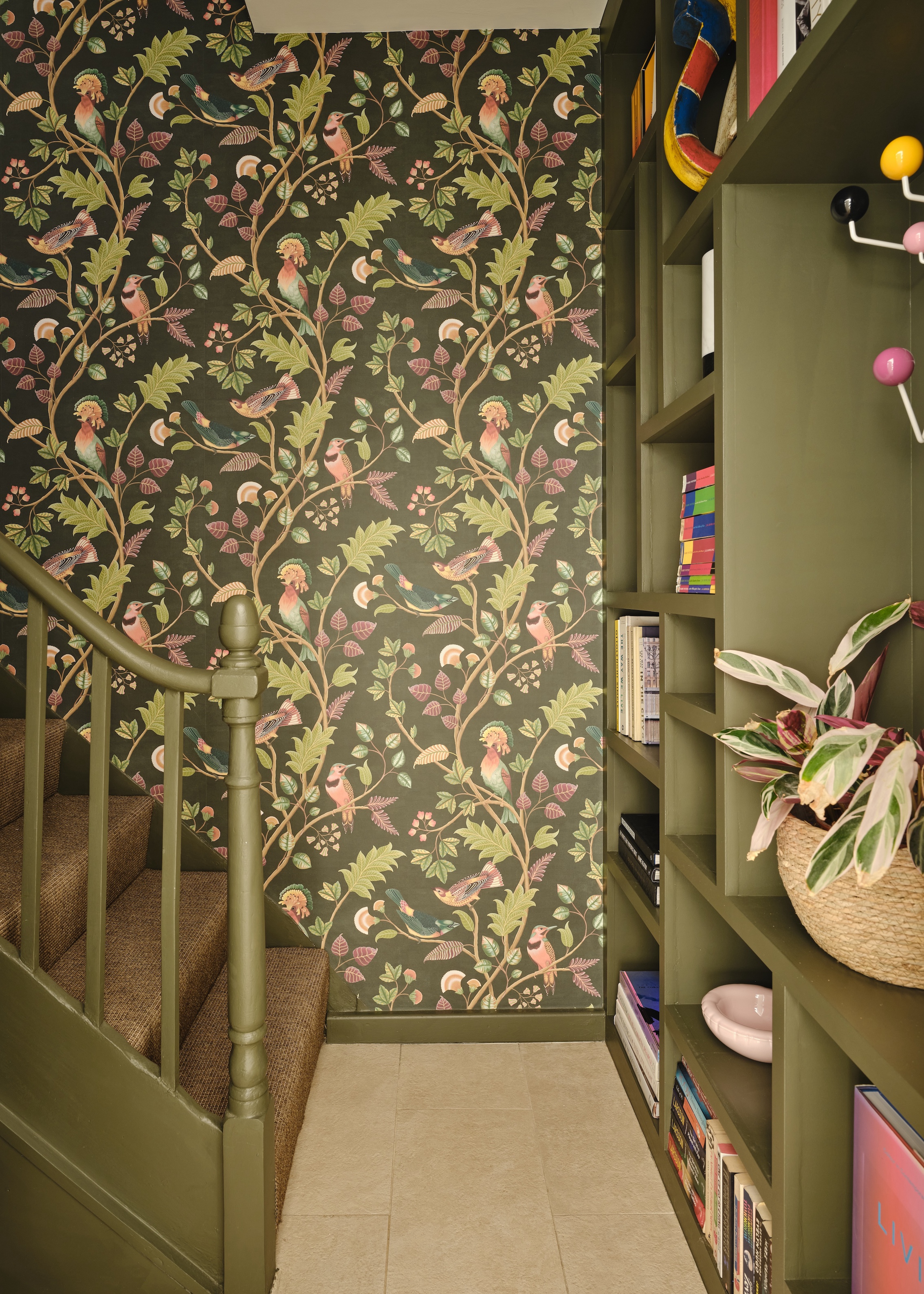 Hallway with bespoke storage and bannisters painted olive green and botanical wallpaper