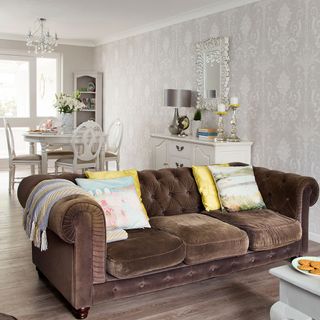 living room with grey designed wall brown sofa with cushions and wooden flooring