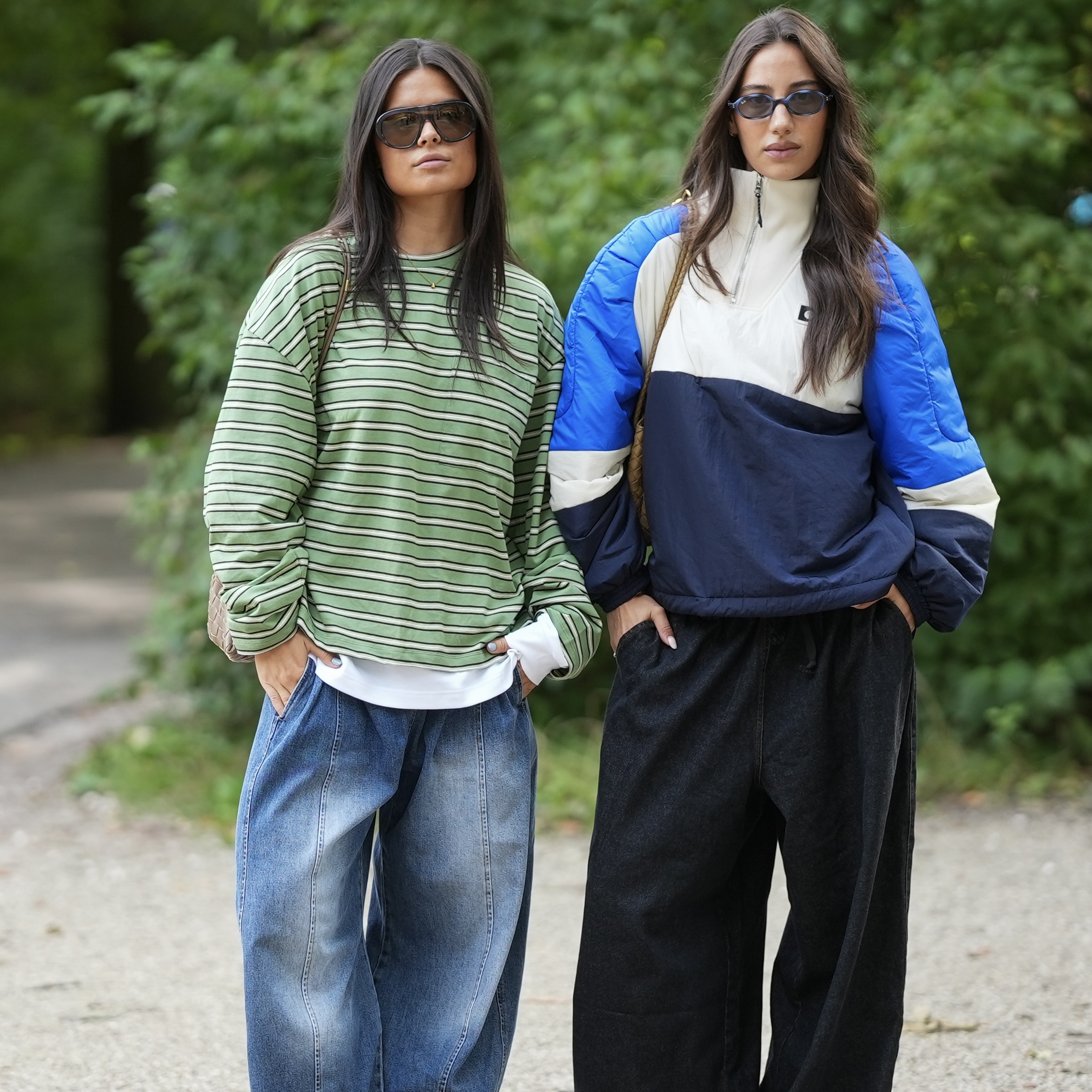 woman wearing a striped green oversized tshirt and jeans next to a woman wearing a funnel neck blue and white color blocked windbreaker with black trousers
