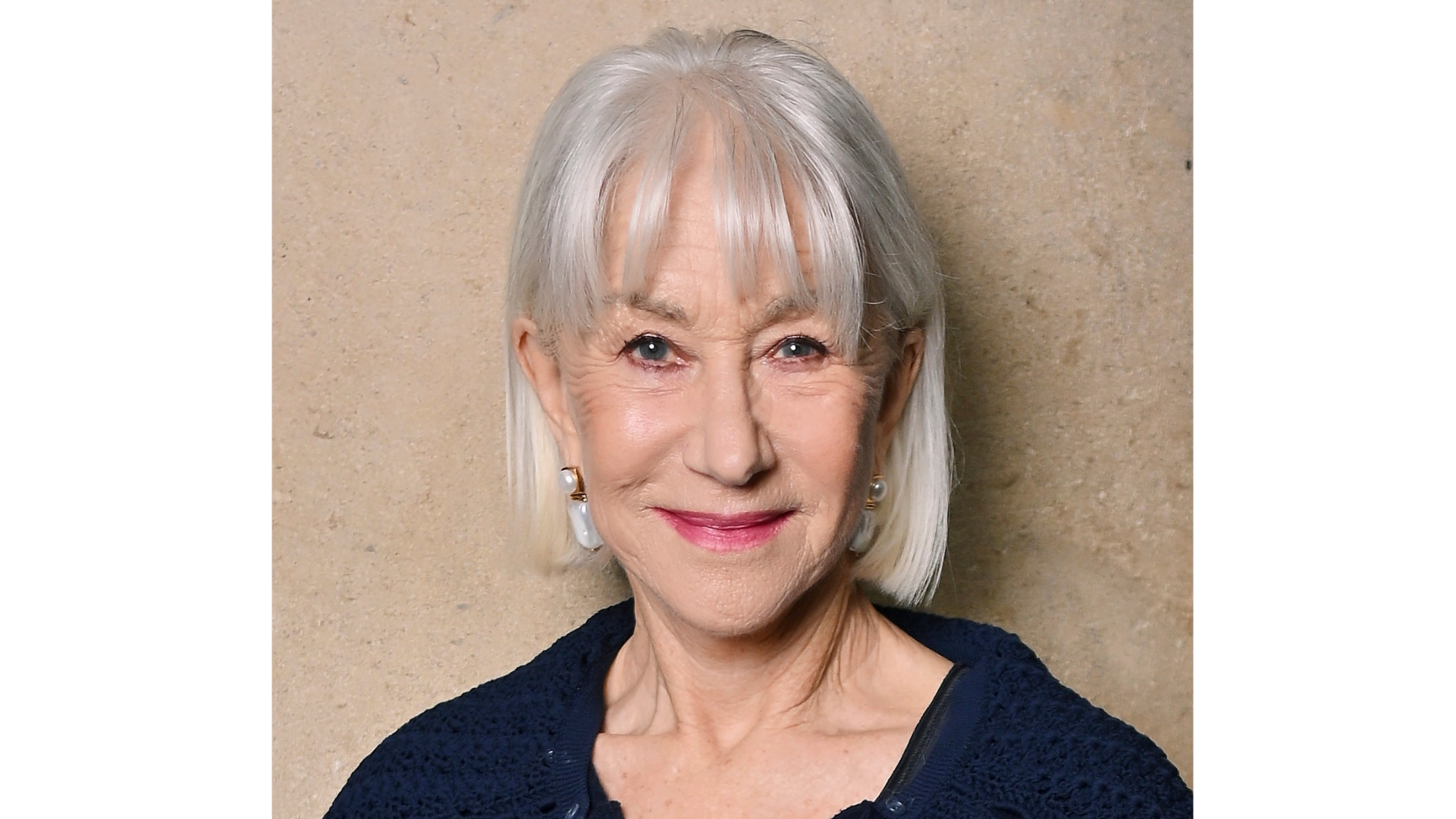 Image of Helen Mirren smiling with silver bob with a fringe, wearing a navy dress and magenta pink lipstick