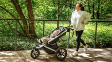 A woman runs along a wooden path pushing a baby in a three-wheeled stroller.