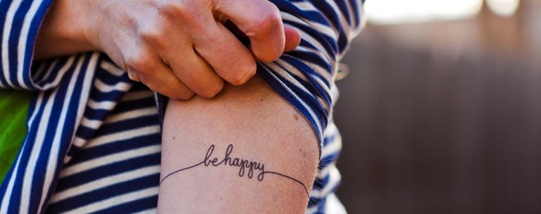 micro tattoos - woman's arm with "be happy" on it as a tattoo