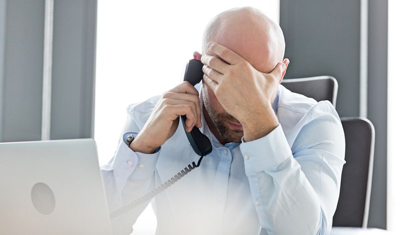 A man holding his face while on a landline phone call