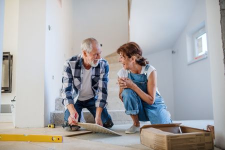 Couple laying tile floor in new home. 