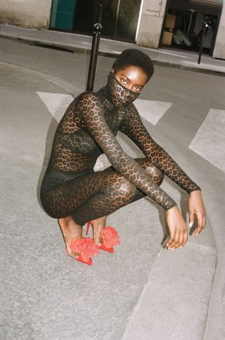 Model wears sheer black body suit and red shoes