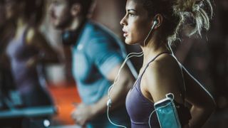 Here is a roundup of the best running headphones. Shown here, the profile of a woman on a treadmill wearing wired in-the-ear headphones.