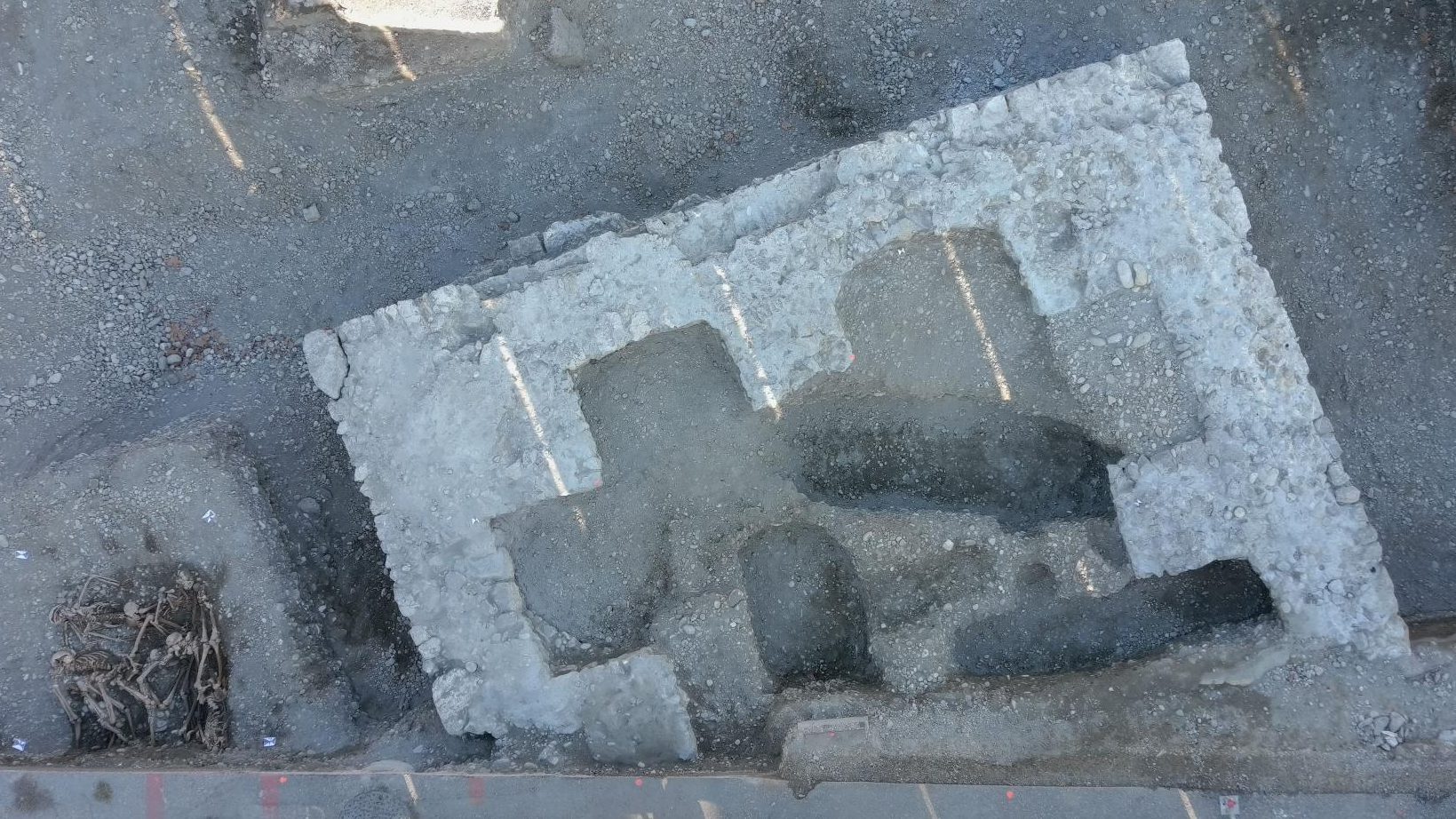 aerial view of an archaeological excavation featuring a square structure and a pit of human remains