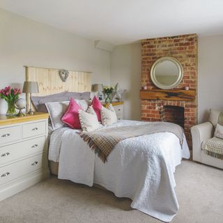 Neutral bedroom with wooden headboard and fireplace with brick detailing and round mirror