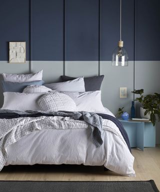 A blue bedroom with wall paneling decor and bed with white seersucker bedding decor