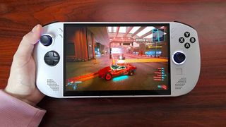 Hand holding Lenovo Legion Go S handheld on woodgrain desk with Cyberpunk 2077 gameplay on screen.