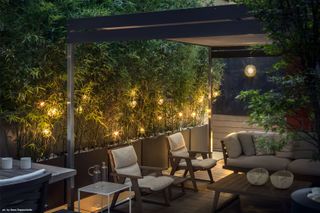 outdoor seating area under a pergola and surrounded by garden lighting
