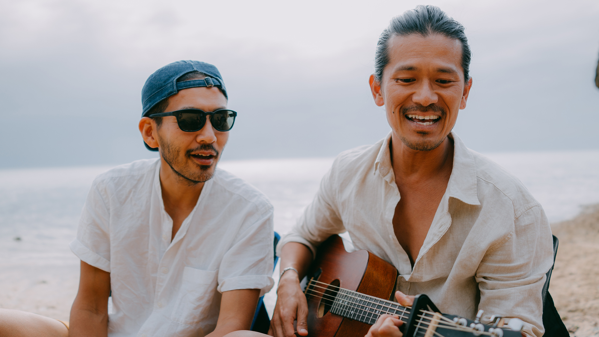 Two men sing while the one on the right plays the guitar
