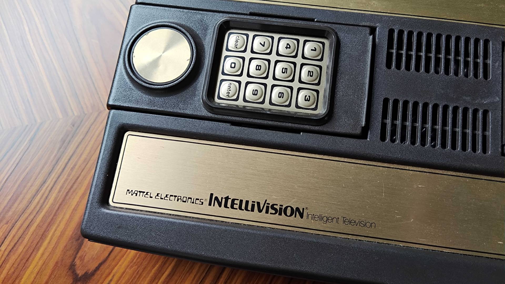 Close up of Mattel Intellivision original console logo on gold decal that reads "Mattel Electronics Intellivision intellegent television on woodgrain table.