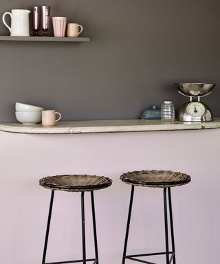 small curved wooden shelf on wall painted pink on lower half and brown above with two wooden stools for a dining area