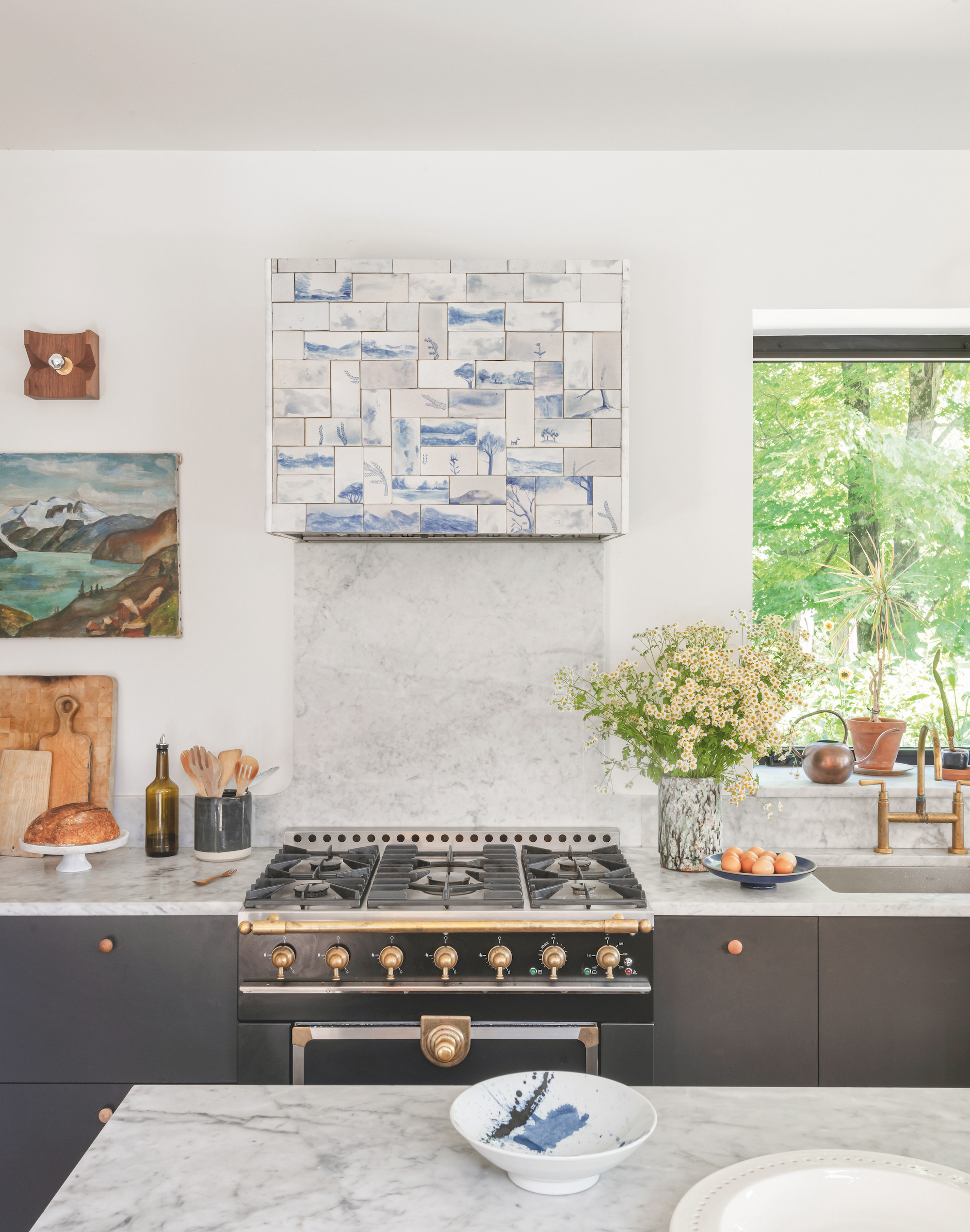 A white walled kitchen with a view of the hob and oven. The island, worktops and backsplash are all white marble and there is a blue and marble tile over the extractor above the hob.