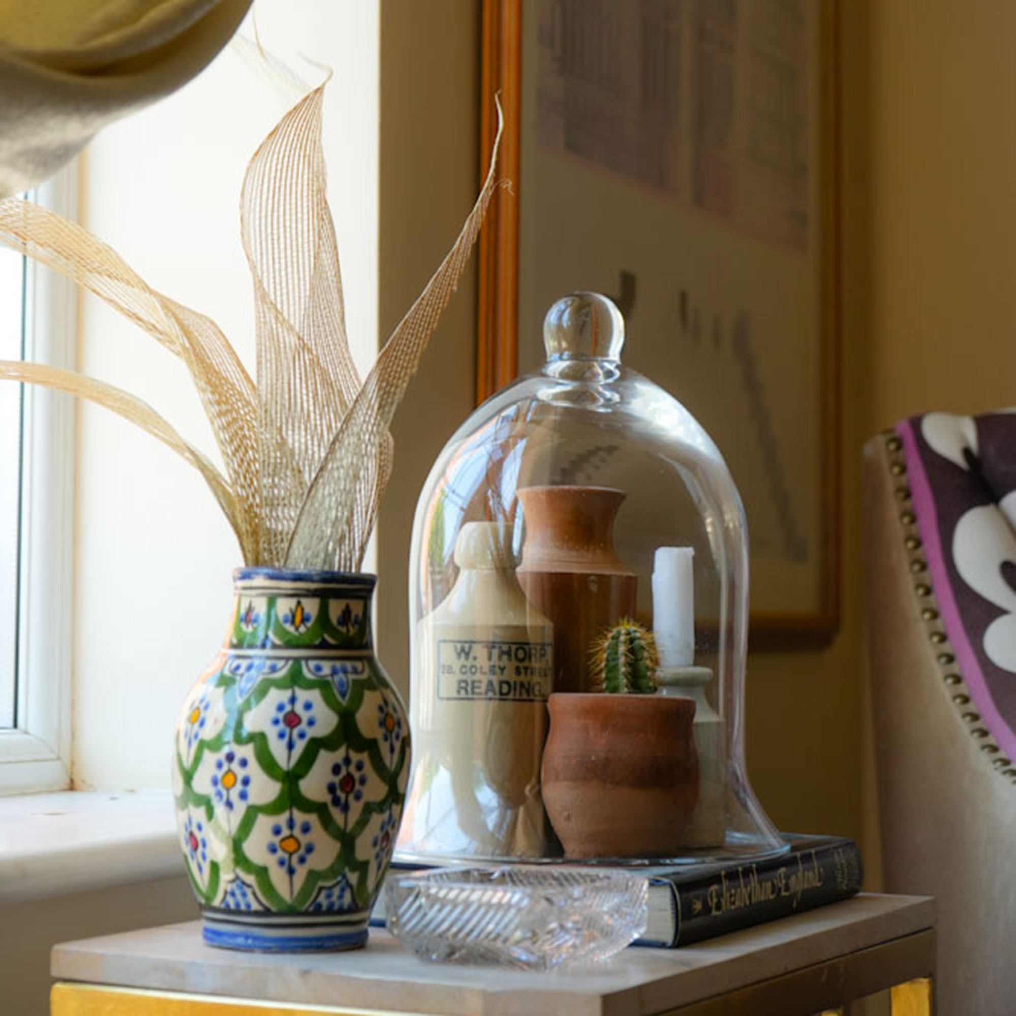 Ceramic jars and cactus under glass cloche beside patterned vase with fabric flowers