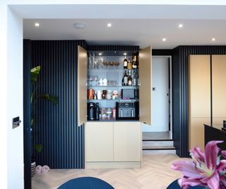 kitchen with black and light wood units with door open showing contents of pantry style floor to ceiling cupboard and false doors below closed