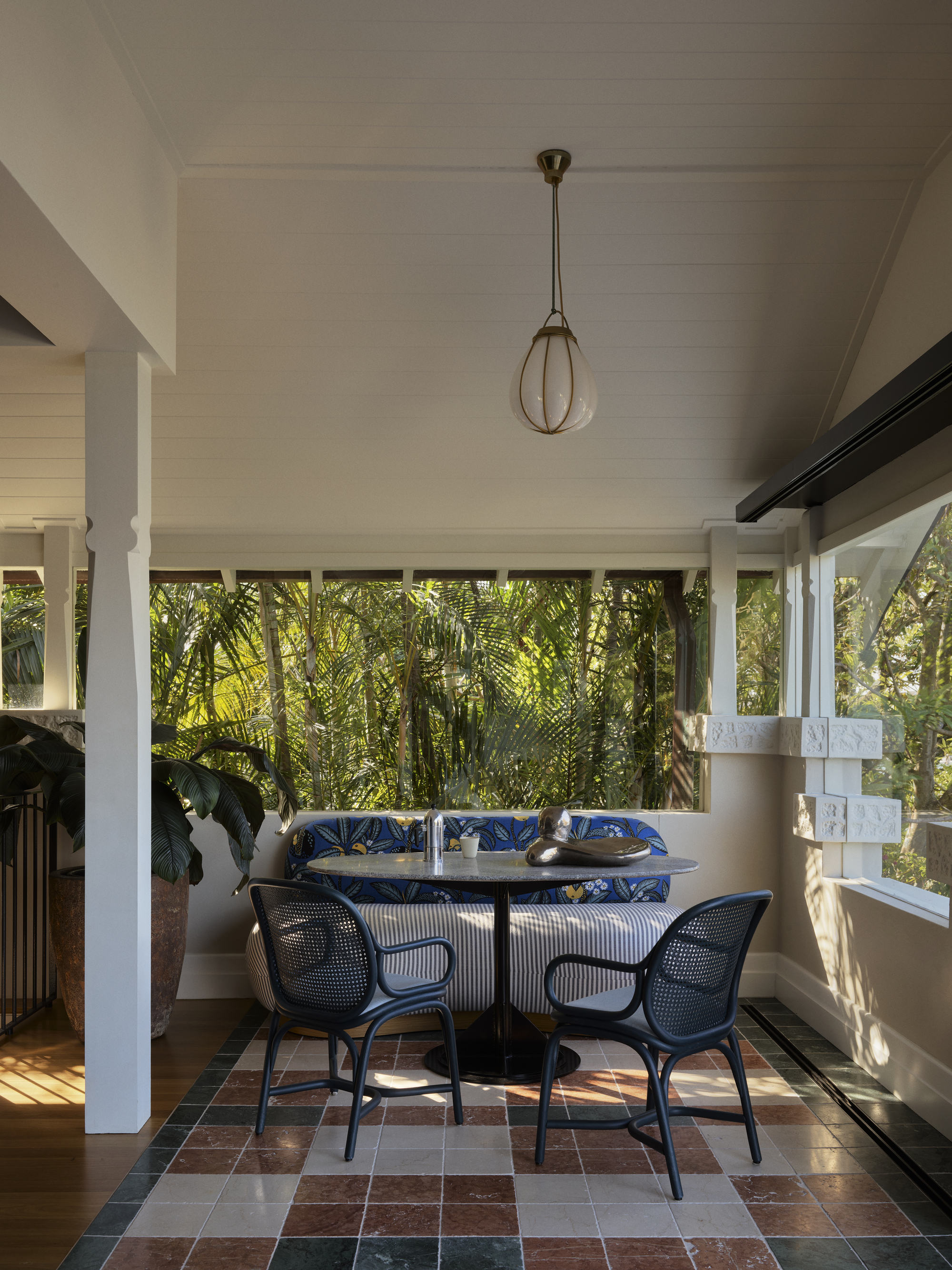 modern sunroom enclosed in glass, with tiled floor, sofa, table, and two armchairs, and the floor transitions to timber in the main part of the home