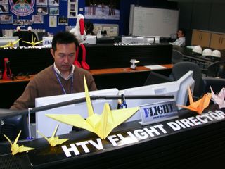 Kota Tanabe is pictured at his HTV console at the Tsukuba Space Center in Japan. Sitting atop the console are two examples of a large number of origami cranes that were distributed in the control rooms in both Houston and Japan. Meantime the Expedition 27 crew onboard the International Space Station joined them in paying tribute to the Japanese population who suffered from the March 11 earthquake and tsunami