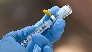 close up of a health care worker&#039;s gloved hands as they draw the jynneos vaccine out of a vial and into a syringe