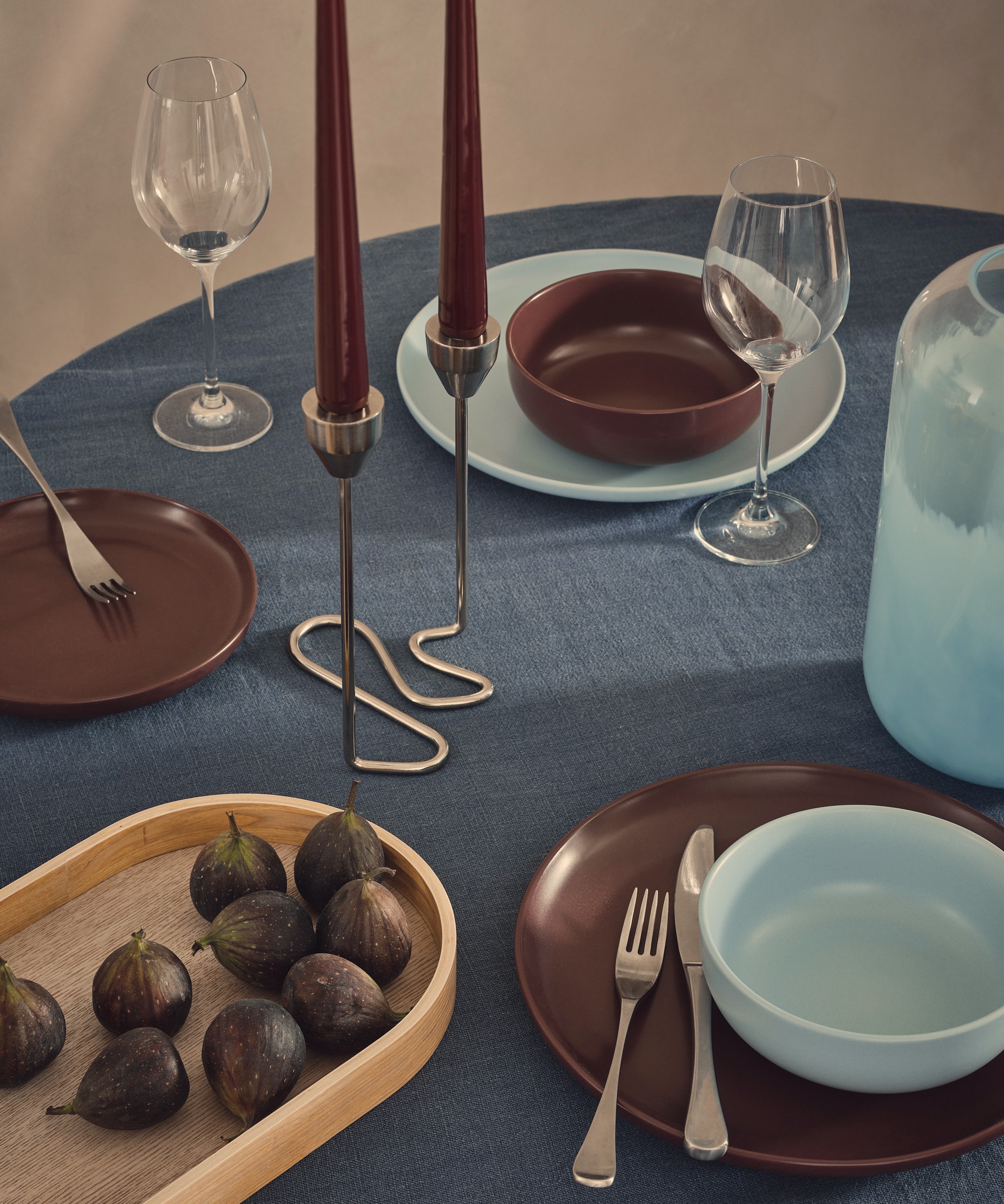 A set table dressed in a blue linen tablecloth with burgundy and sky blue tableware and chrome candelabra with burgundy dinner candles
