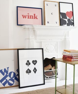 A white living room with white fireplace and assortment of framed slogan wall art by Oliver Bonas