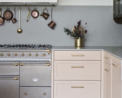 A kitchen with pastel pink cabinets and pans hanging up