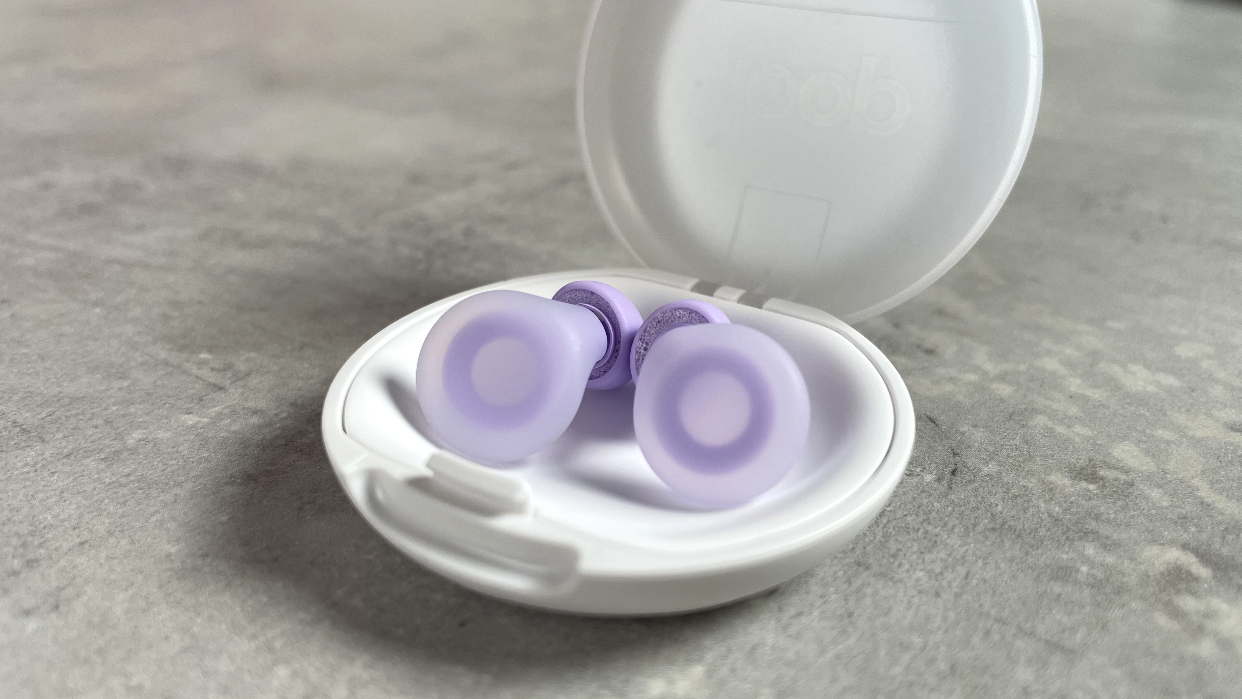 A pair of lilac Loop Dream earplugs are sitting in their white case.