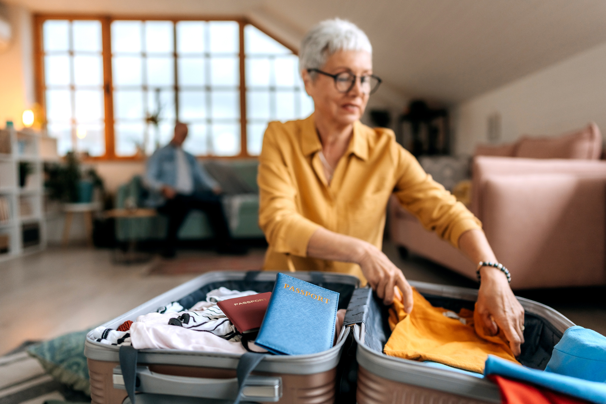 A senior woman packs her suitcase at home.