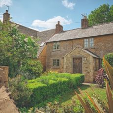 Exterior of bricked cottage house with lots of greenery in the front garden and a wooden door