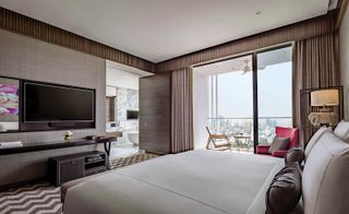 Bedroom in neutral tones with a zig-zag carpet, en-suite bathroom and views over Bangkok