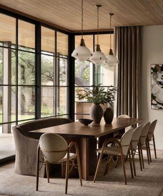 Neutral dining room with wood dining table, boucle chairs and linen sofa, glass pendant lights and large windows