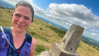 Helen Ryver wearing running clothes on a hill next to a stone monument on top of a hill