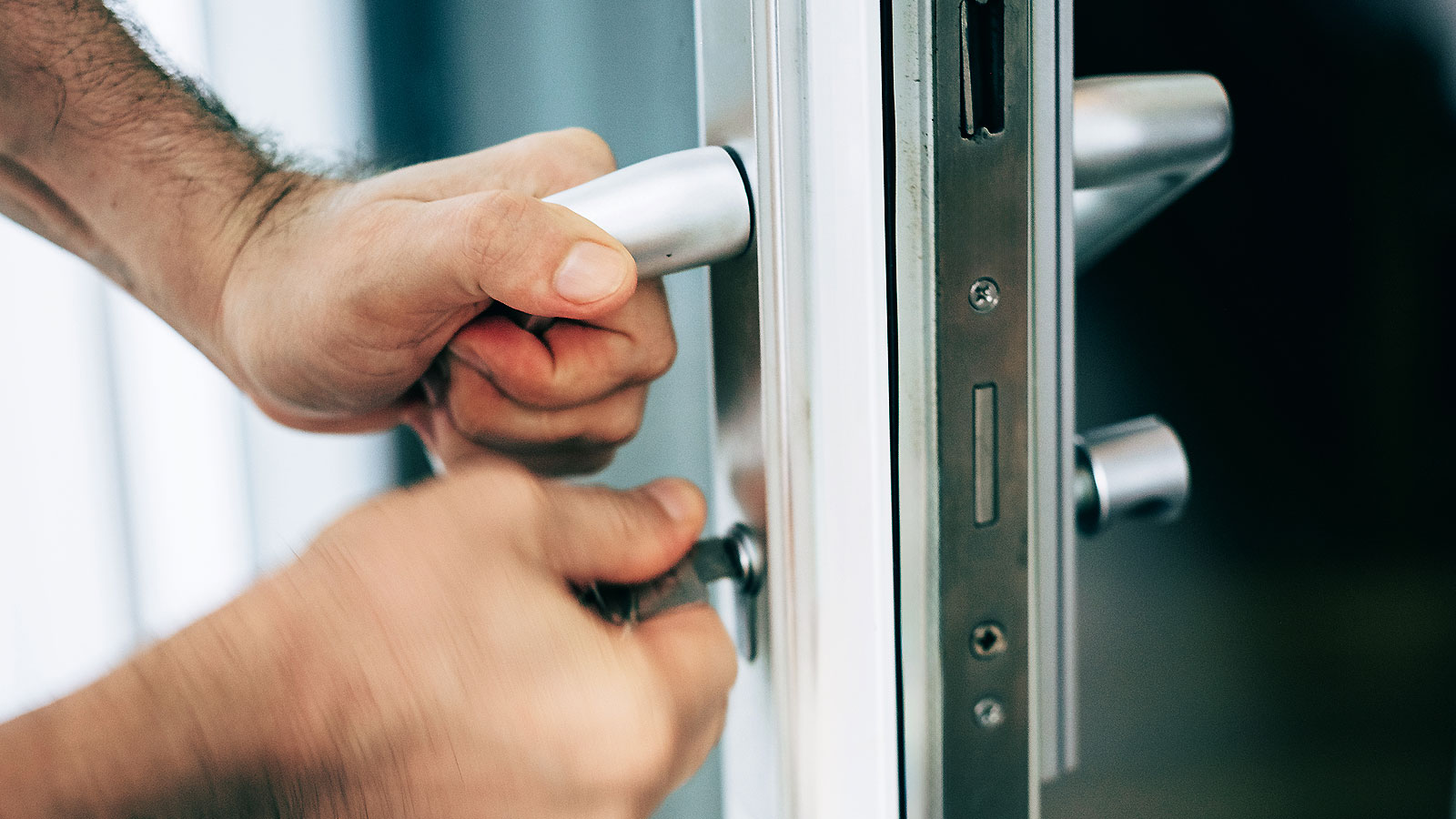 Pair of hands holding handle and turning key on white UPVC door handle and lock 