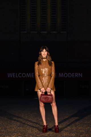 Daisy Edgar-Jones wearing a camel-brown leather minidress with burgundy accessories at the Gucci Cruise 2025 show.