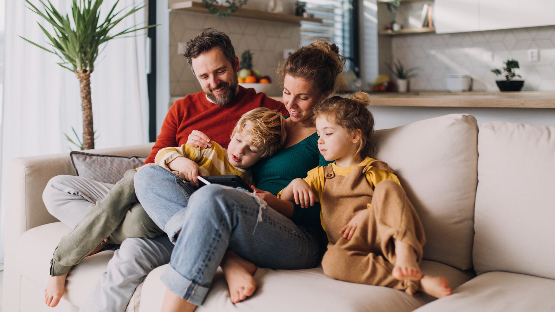 A family of four sits on the sofa, all looking at the same smartphone