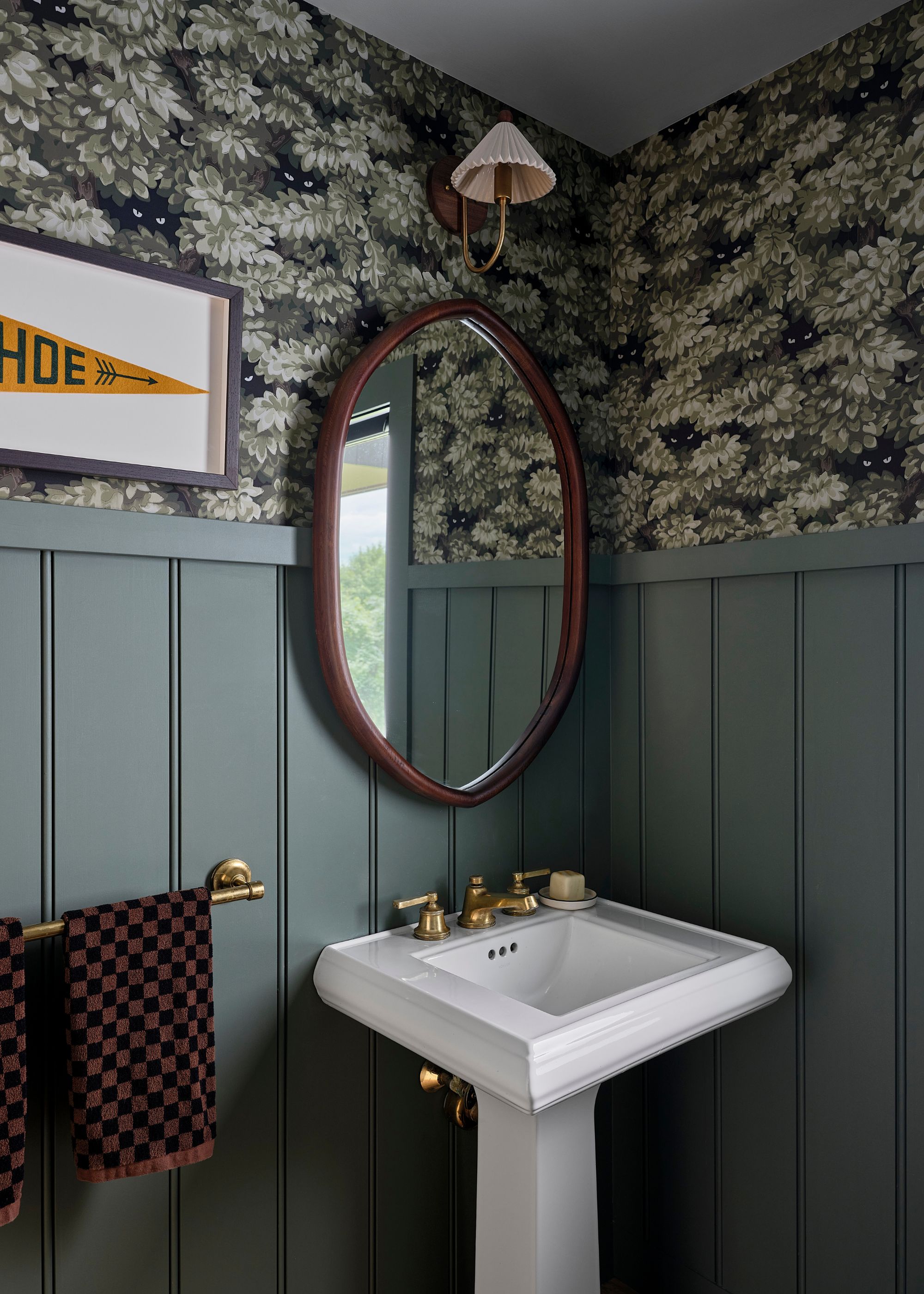 A powder room with dark gray beadboard paneling and floral wallpaper above it. A small white sink and an oval mirror above it.