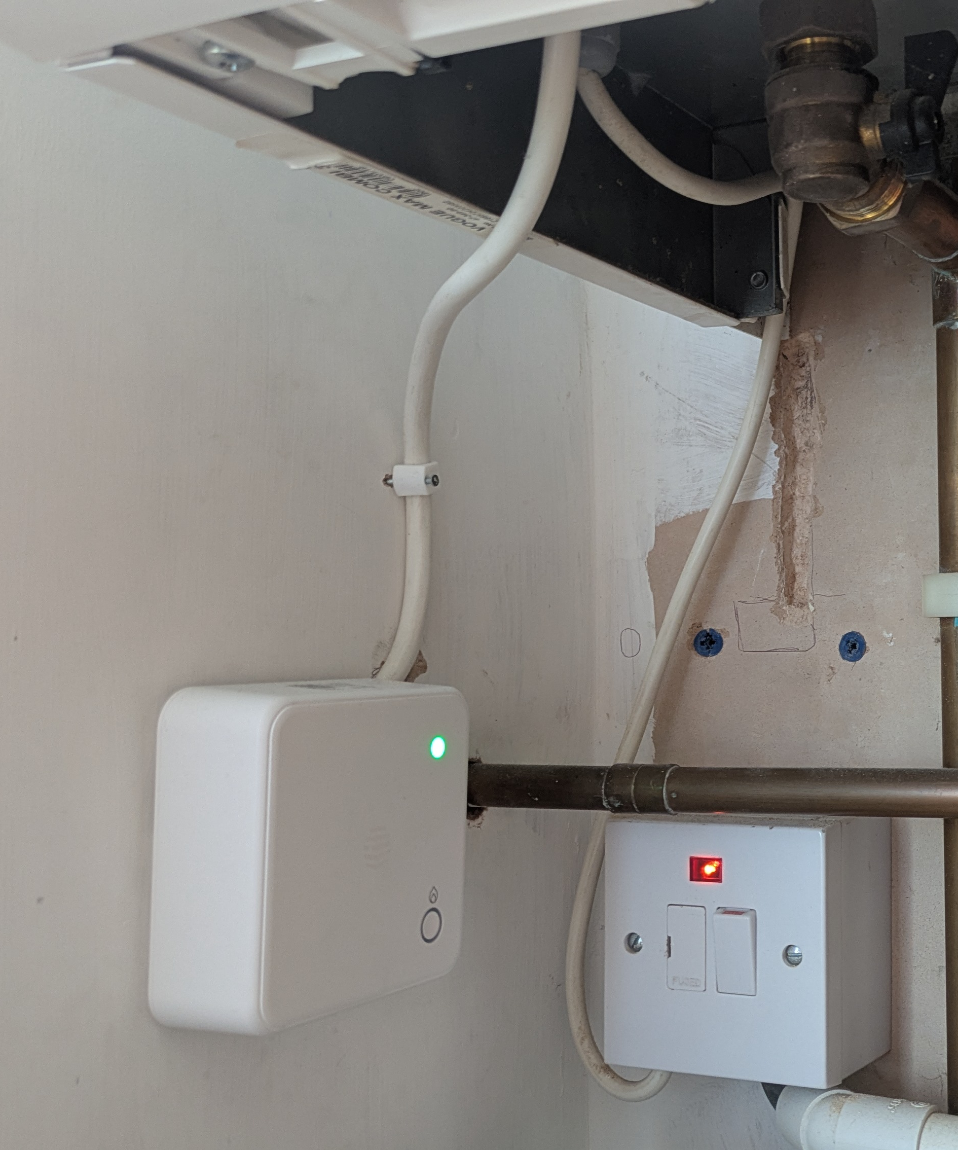 A wall-mounted receiver unit connected by a wire to a combi boiler