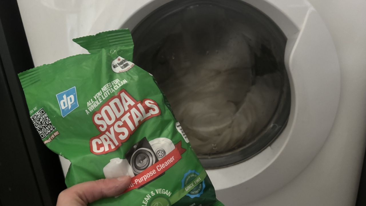 A bag of soda crystals held up to a washing machine drum containing a pillow being washed.
