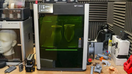 Testing out the Bambu Lab H2D in our workshop, with a vase printing inside, surrounded by other 3D printing accessories and materials